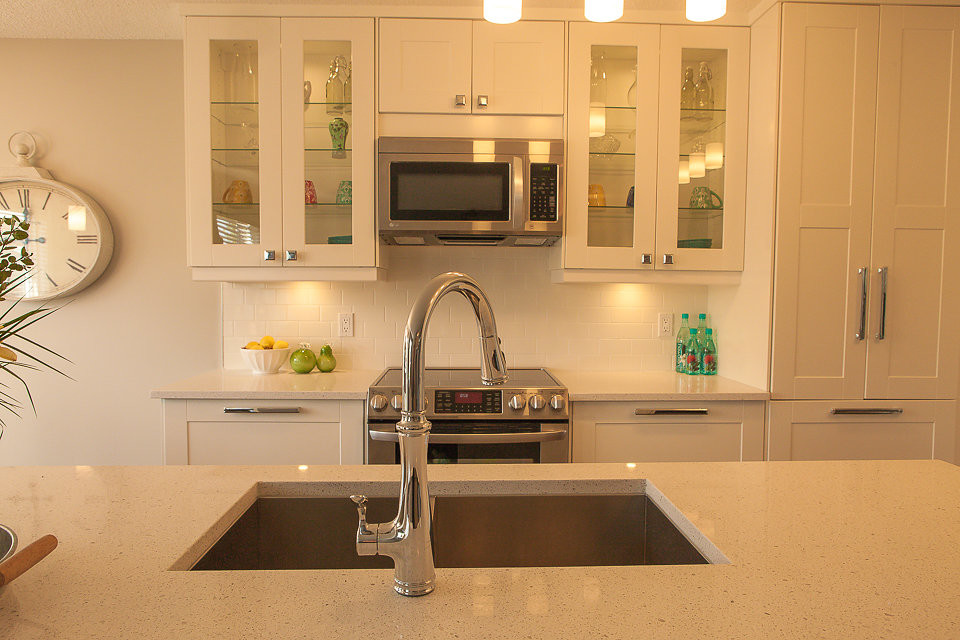 Example of a mid-sized transitional l-shaped medium tone wood floor eat-in kitchen design in Calgary with a double-bowl sink, shaker cabinets, white cabinets, quartzite countertops, white backsplash, ceramic backsplash, stainless steel appliances and an island