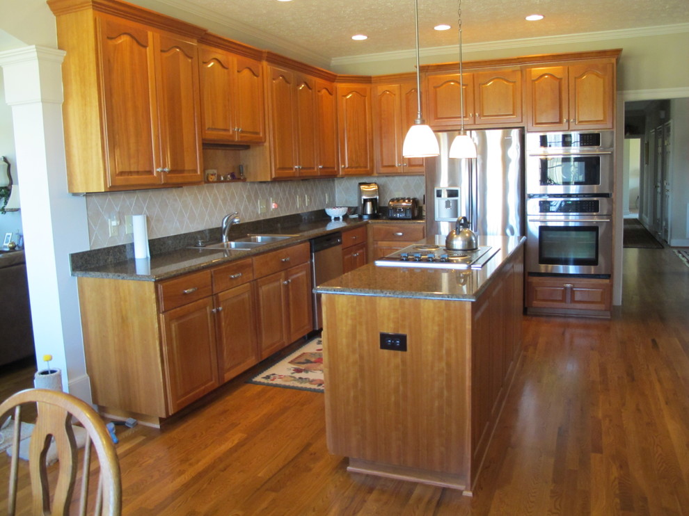 Example of a mid-sized arts and crafts l-shaped medium tone wood floor and beige floor open concept kitchen design in Detroit with a double-bowl sink, raised-panel cabinets, medium tone wood cabinets, granite countertops, beige backsplash, stainless steel appliances and an island