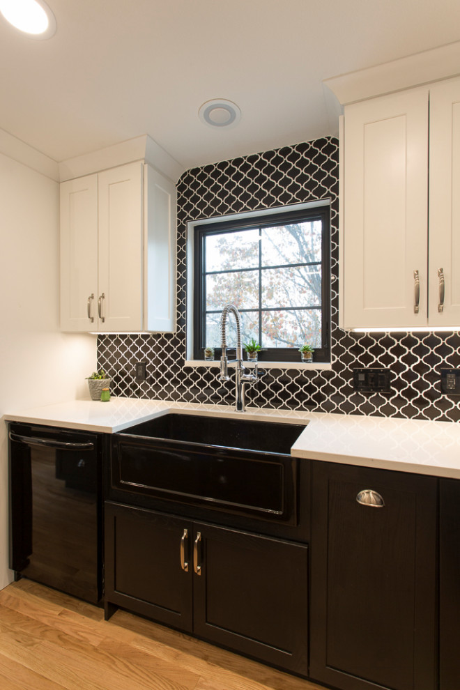 Modern inredning av ett mellanstort vit vitt kök, med en rustik diskho, skåp i shakerstil, svarta skåp, bänkskiva i kvarts, svart stänkskydd, stänkskydd i mosaik, svarta vitvaror, ljust trägolv, en köksö och brunt golv