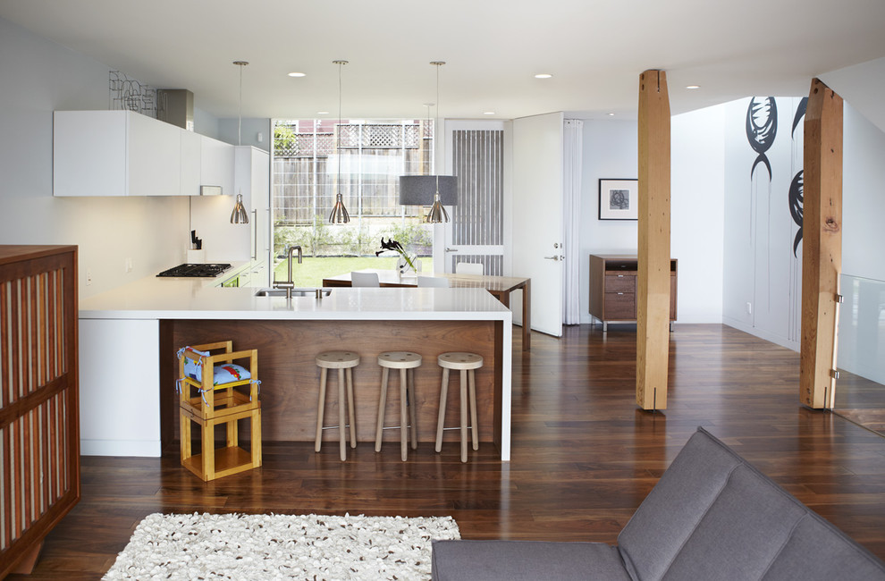 На фото: угловая кухня-гостиная в стиле модернизм с врезной мойкой, плоскими фасадами и белыми фасадами