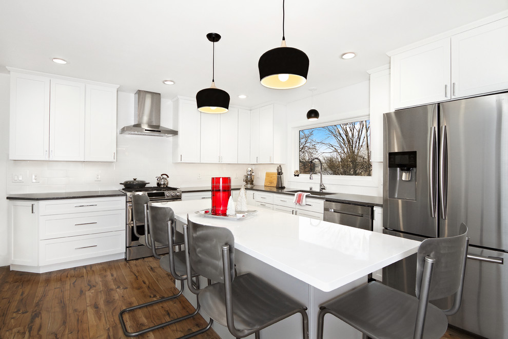 Example of a transitional l-shaped dark wood floor kitchen design in Other with white cabinets, quartz countertops, white backsplash, an undermount sink, shaker cabinets, subway tile backsplash, stainless steel appliances, an island and black countertops