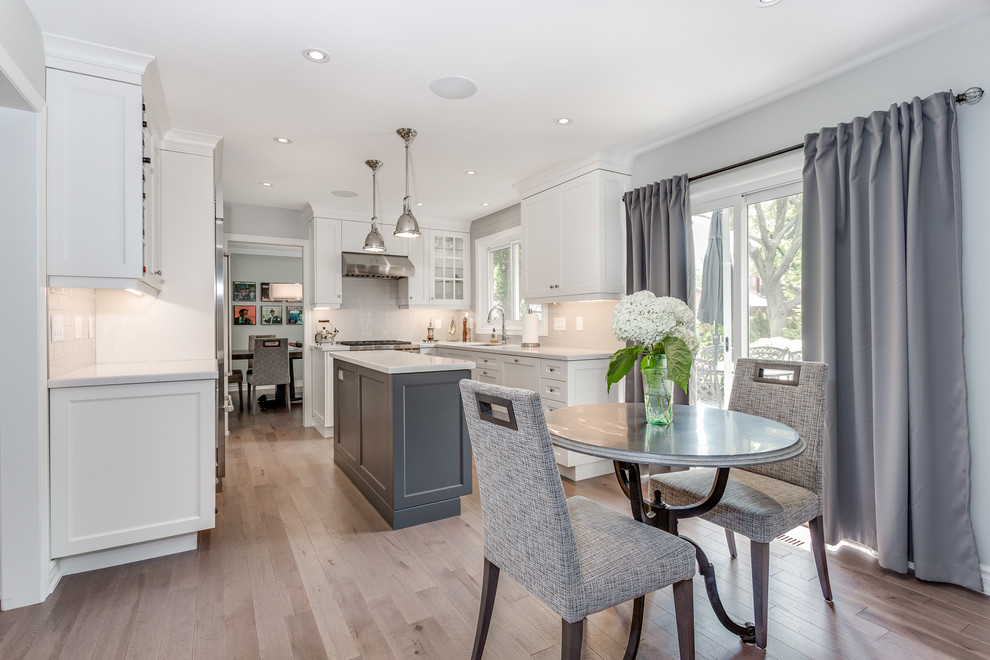 Eat-in kitchen - large transitional l-shaped dark wood floor and brown floor eat-in kitchen idea in Toronto with an undermount sink, shaker cabinets, white cabinets, quartzite countertops, white backsplash, subway tile backsplash, stainless steel appliances and an island