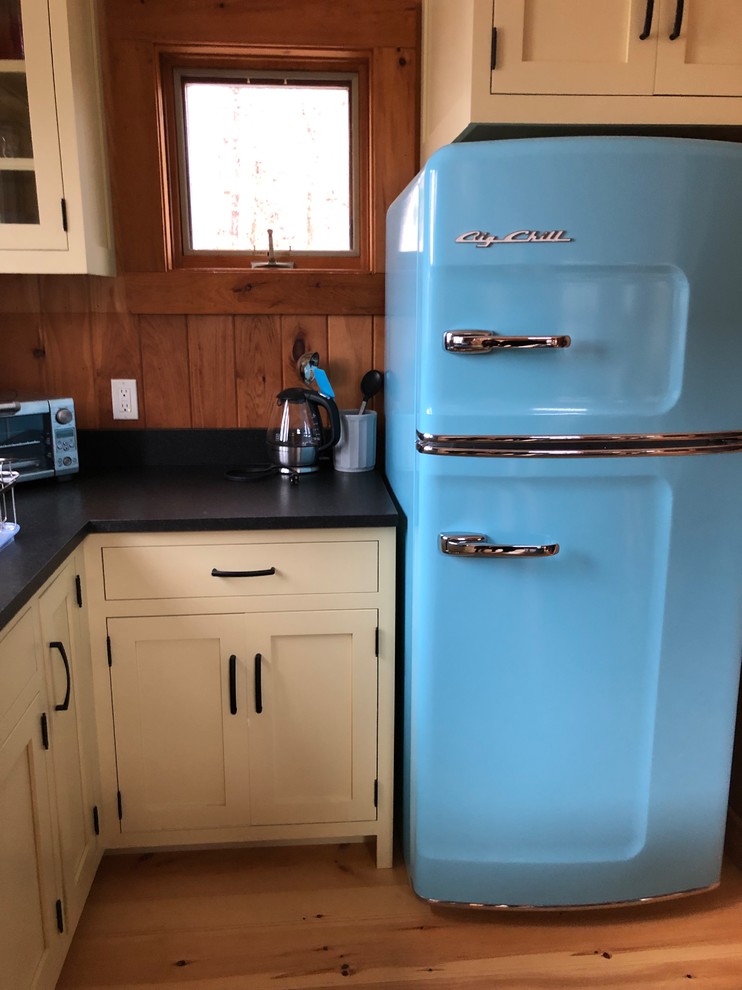 Urige Küche mit Einbauwaschbecken, Schrankfronten im Shaker-Stil, gelben Schränken, Granit-Arbeitsplatte, bunten Elektrogeräten, hellem Holzboden, Kücheninsel, beigem Boden und schwarzer Arbeitsplatte in Portland Maine