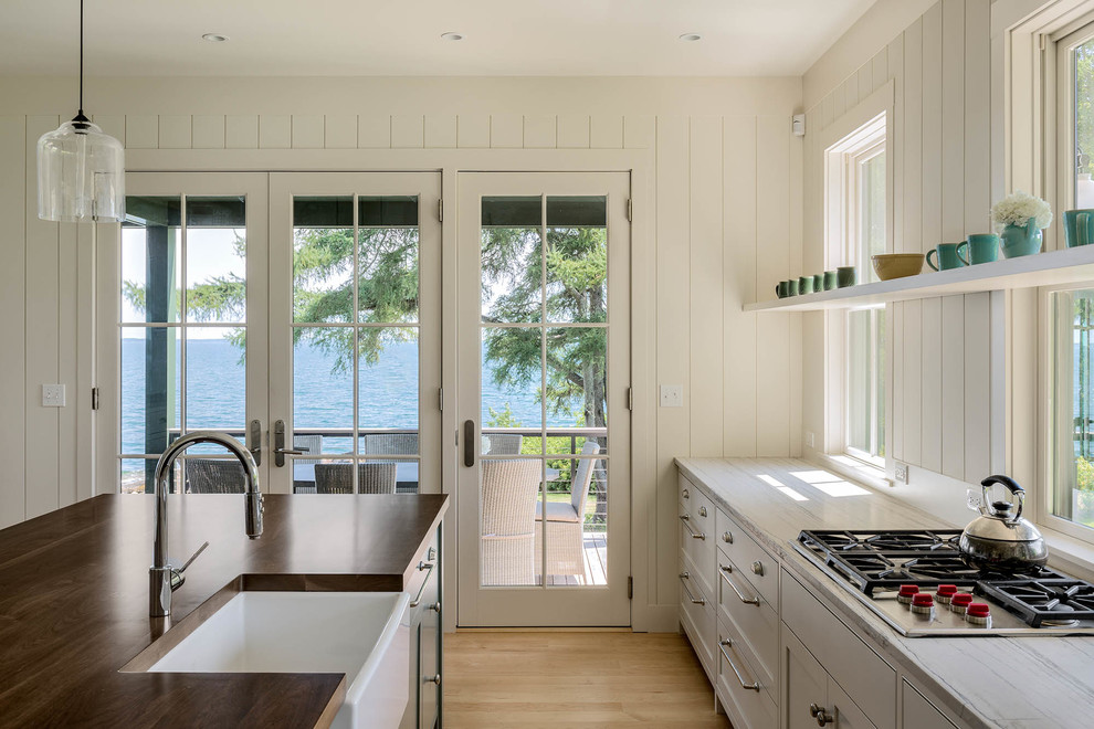 Eat-in kitchen - mid-sized coastal galley light wood floor eat-in kitchen idea in Portland Maine with a single-bowl sink, shaker cabinets, white cabinets, wood countertops, white backsplash, stainless steel appliances and an island