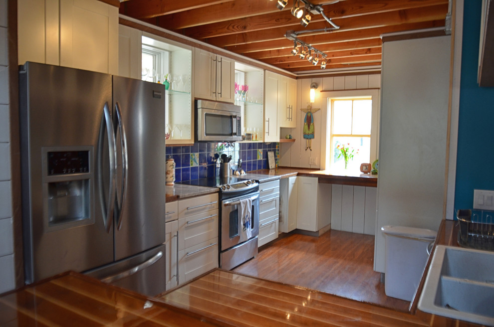 This is an example of a medium sized nautical l-shaped open plan kitchen in Portland Maine with a double-bowl sink, flat-panel cabinets, white cabinets, wood worktops, blue splashback, stainless steel appliances, medium hardwood flooring and an island.