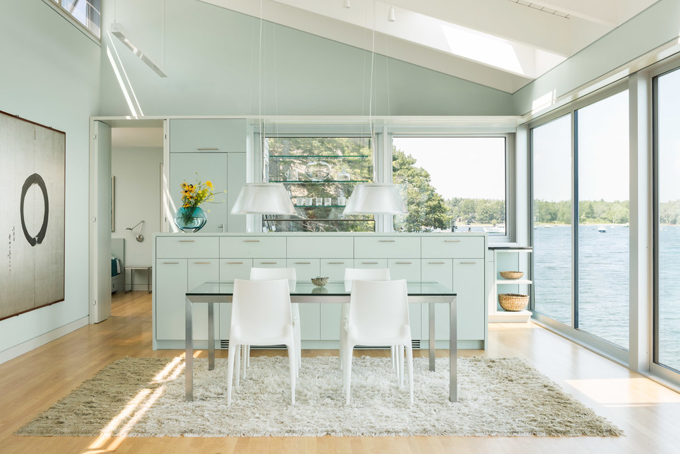 Ejemplo de cocina contemporánea con una isla, armarios con paneles lisos, puertas de armario azules, salpicadero de vidrio, suelo de madera clara y suelo beige