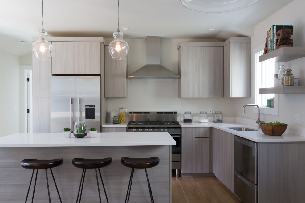 Foto på ett funkis vit l-kök, med en undermonterad diskho, släta luckor, grå skåp, rostfria vitvaror, mellanmörkt trägolv, en köksö och brunt golv