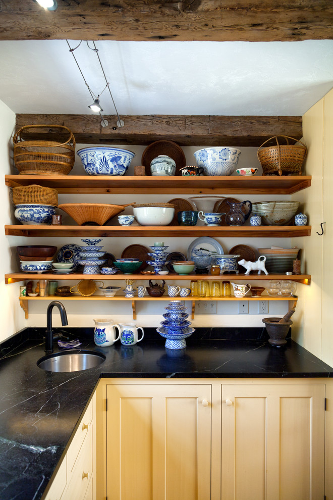 Foto på ett lantligt kök, med en undermonterad diskho, öppna hyllor och gula skåp