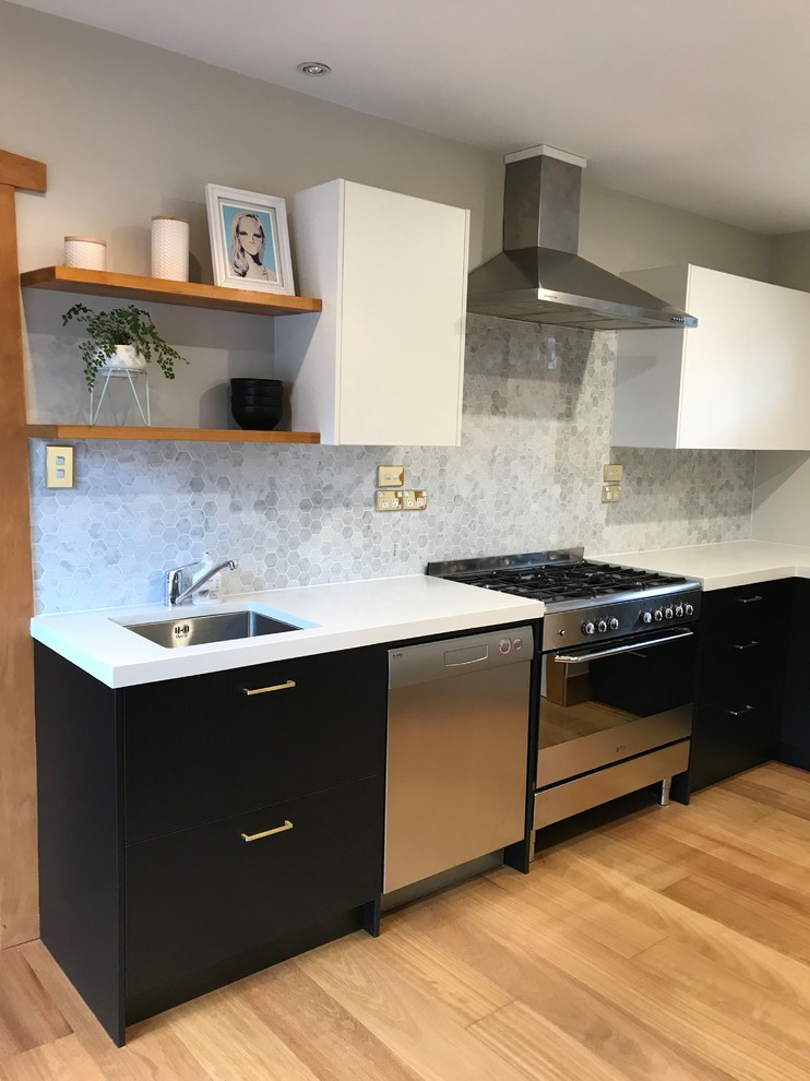 Photo of a medium sized contemporary l-shaped enclosed kitchen in Christchurch with a single-bowl sink, flat-panel cabinets, black cabinets, concrete worktops, grey splashback, mosaic tiled splashback, stainless steel appliances, light hardwood flooring, no island, brown floors and white worktops.