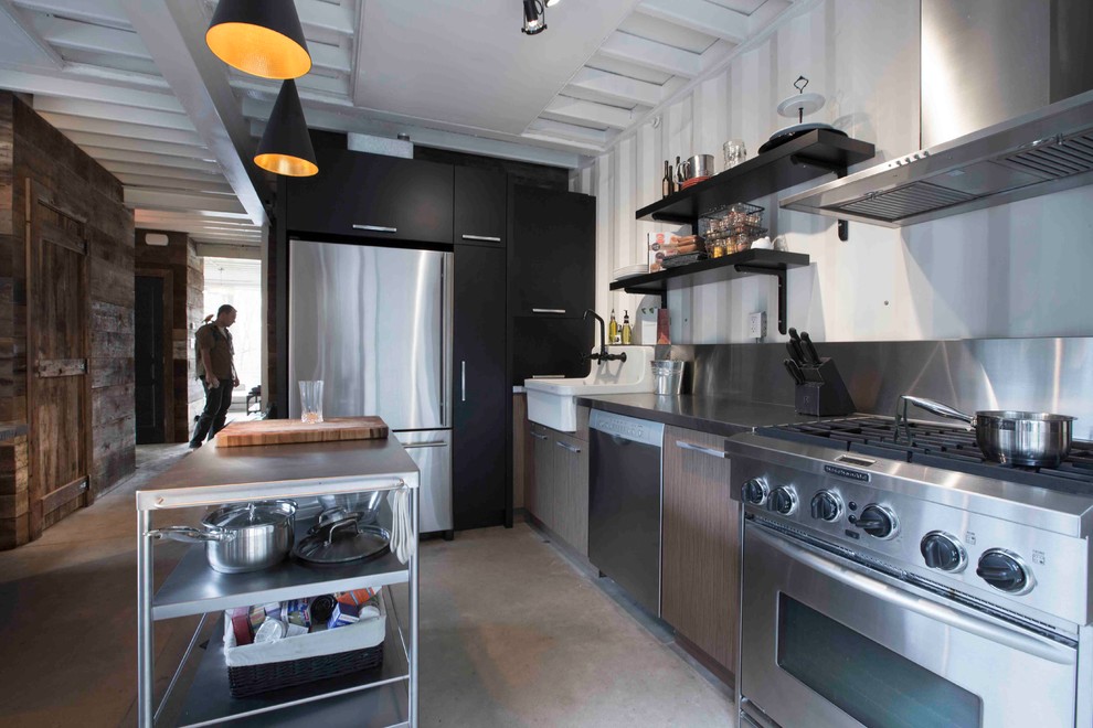 Bild på ett industriellt kök, med en rustik diskho, bruna skåp, bänkskiva i rostfritt stål, vitt stänkskydd, stänkskydd i metallkakel och rostfria vitvaror