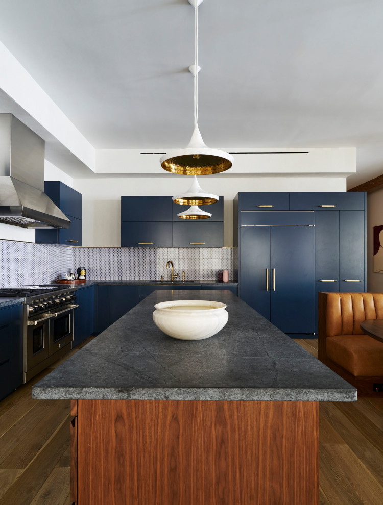 Cette photo montre une cuisine américaine encastrable tendance en L avec un évier encastré, un placard à porte plane, des portes de placard bleues, une crédence bleue, une crédence en mosaïque, un sol en bois brun, îlot, un sol marron et un plan de travail gris.