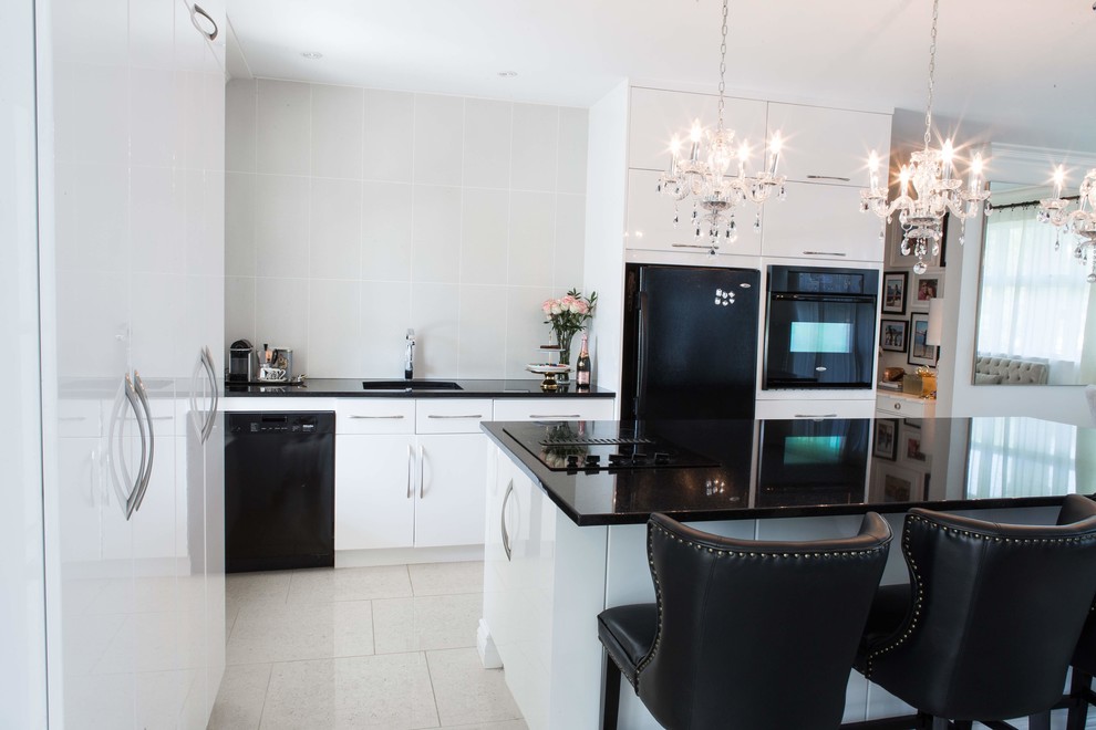 Large modern galley kitchen/diner in Montreal with a submerged sink, flat-panel cabinets, white cabinets, granite worktops, white splashback, porcelain splashback, black appliances, porcelain flooring, an island, beige floors and black worktops.