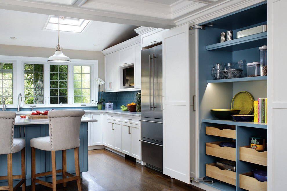Inspiration for a large transitional u-shaped medium tone wood floor kitchen pantry remodel in New York with an undermount sink, recessed-panel cabinets, white cabinets, blue backsplash, glass tile backsplash, stainless steel appliances and an island