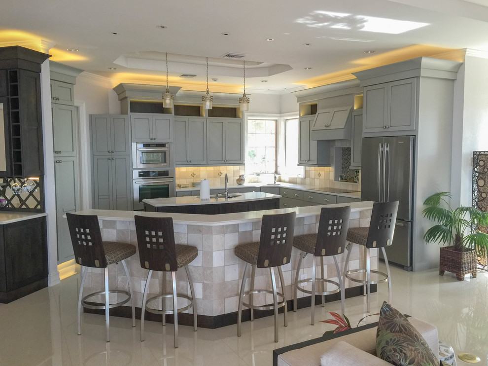 This is an example of a large contemporary l-shaped open plan kitchen in Miami with a submerged sink, shaker cabinets, grey cabinets, engineered stone countertops, beige splashback, stone tiled splashback, stainless steel appliances, porcelain flooring and multiple islands.