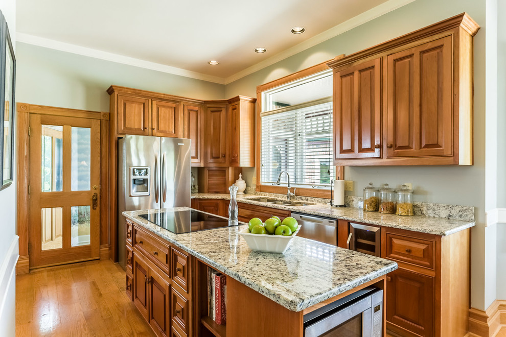 This is an example of a classic kitchen in Kansas City with raised-panel cabinets, medium wood cabinets, granite worktops, stainless steel appliances, medium hardwood flooring and an island.