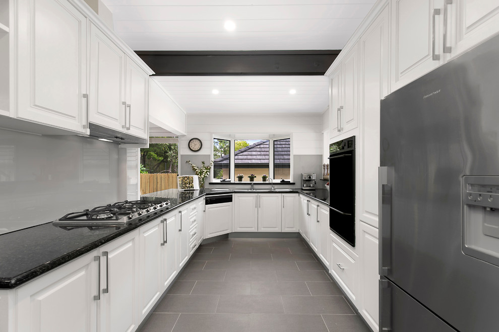 シドニーにあるトランジショナルスタイルのおしゃれなキッチン (ドロップインシンク、レイズドパネル扉のキャビネット、白いキャビネット、グレーのキッチンパネル、ガラス板のキッチンパネル、シルバーの調理設備、アイランドなし、グレーの床) の写真