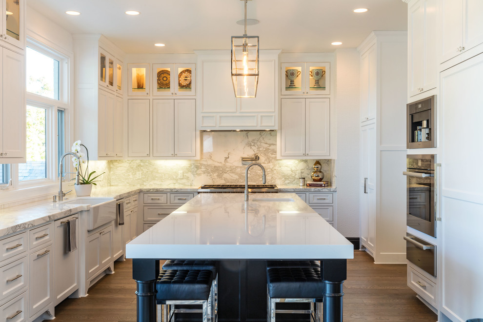 Inspiration for a large traditional u-shaped kitchen in Los Angeles with a belfast sink, stainless steel appliances, an island, beaded cabinets, white cabinets, white splashback, stone slab splashback, dark hardwood flooring and brown floors.