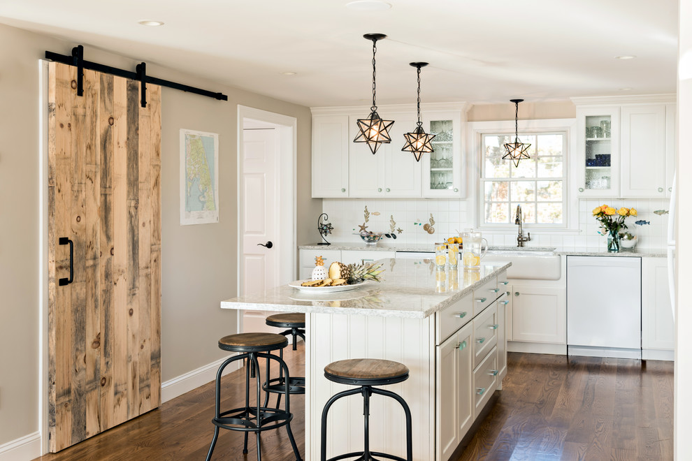 Mid-sized beach style l-shaped dark wood floor and brown floor enclosed kitchen photo in Boston with a farmhouse sink, white cabinets, white backsplash, white appliances, an island, glass-front cabinets, beige countertops, granite countertops and ceramic backsplash