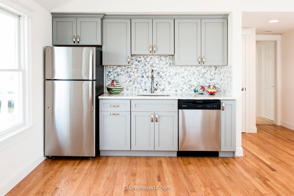 Example of a small beach style single-wall medium tone wood floor open concept kitchen design in New York with an undermount sink, recessed-panel cabinets, gray cabinets, limestone countertops, multicolored backsplash, ceramic backsplash, stainless steel appliances and no island