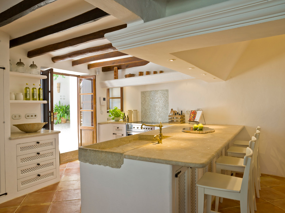 Cette image montre une cuisine méditerranéenne avec un évier intégré, des portes de placard blanches et tomettes au sol.