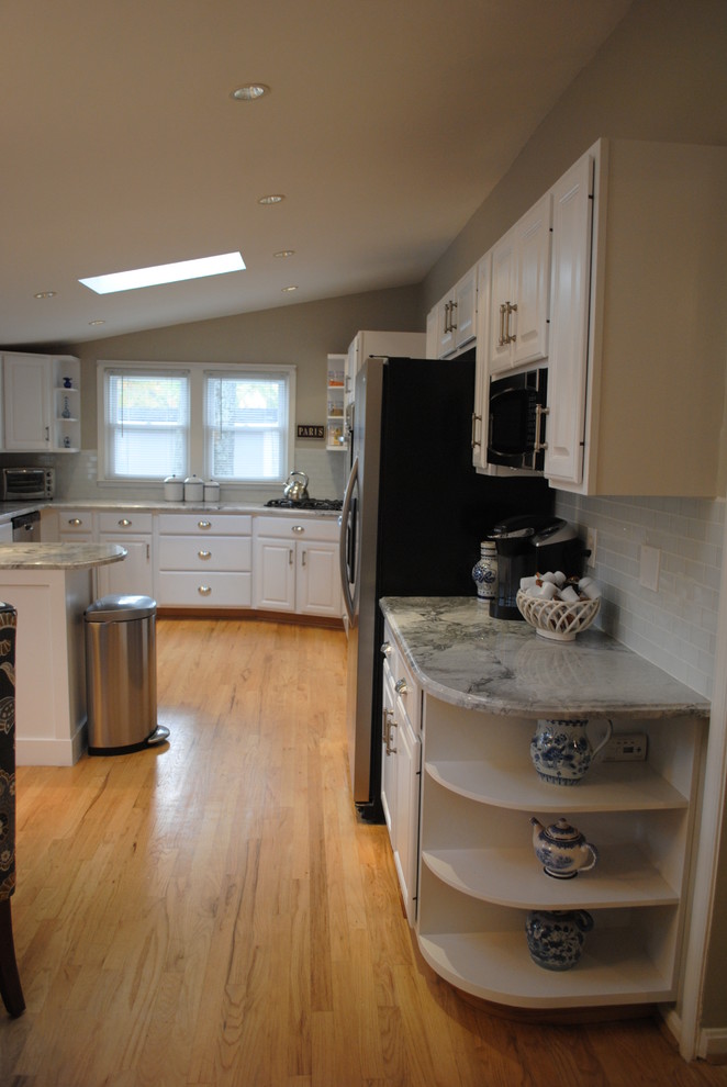 Bild på ett stort lantligt kök, med en undermonterad diskho, luckor med upphöjd panel, vita skåp, granitbänkskiva, vitt stänkskydd, glaspanel som stänkskydd, rostfria vitvaror, ljust trägolv och en halv köksö