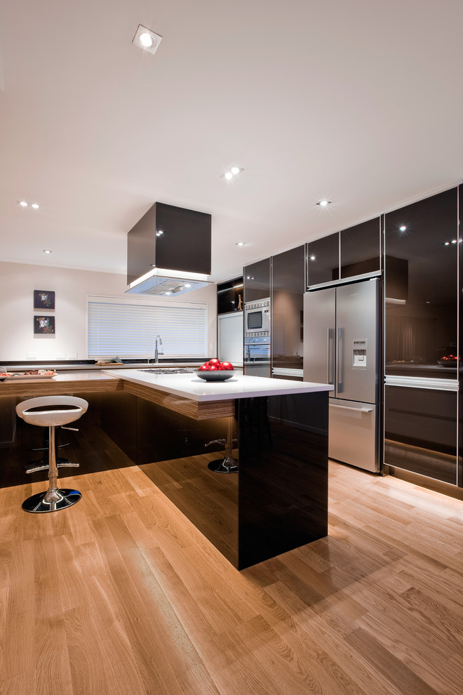 Bild på ett avskilt, mellanstort funkis l-kök, med en undermonterad diskho, släta luckor, svarta skåp, bänkskiva i kvarts, rostfria vitvaror, ljust trägolv, en köksö och beiget golv