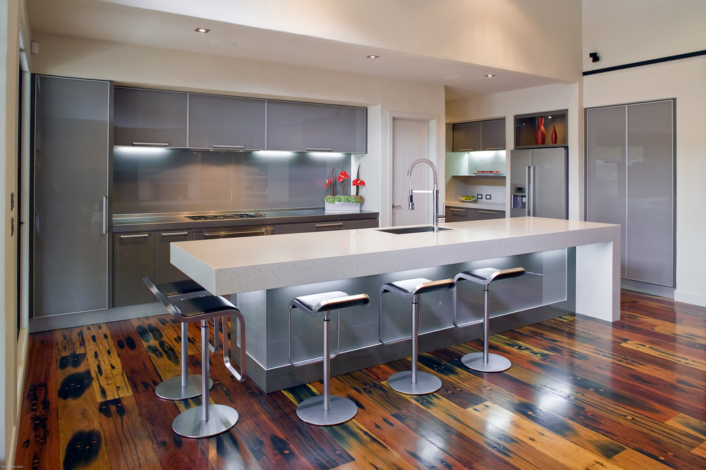 Idéer för mellanstora funkis linjära kök med öppen planlösning, med en undermonterad diskho, luckor med glaspanel, grå skåp, bänkskiva i kvarts, grått stänkskydd, glaspanel som stänkskydd, integrerade vitvaror, mellanmörkt trägolv, en köksö och brunt golv