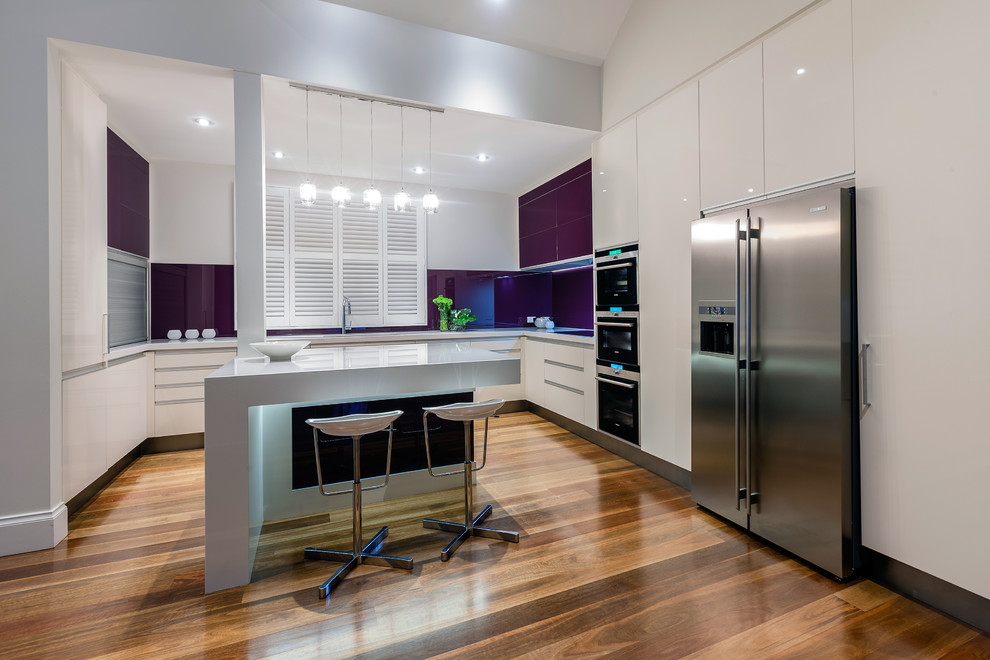 This is an example of a medium sized modern u-shaped kitchen/diner in Los Angeles with a submerged sink, flat-panel cabinets, white cabinets, engineered stone countertops, glass sheet splashback, stainless steel appliances, light hardwood flooring, an island and beige floors.
