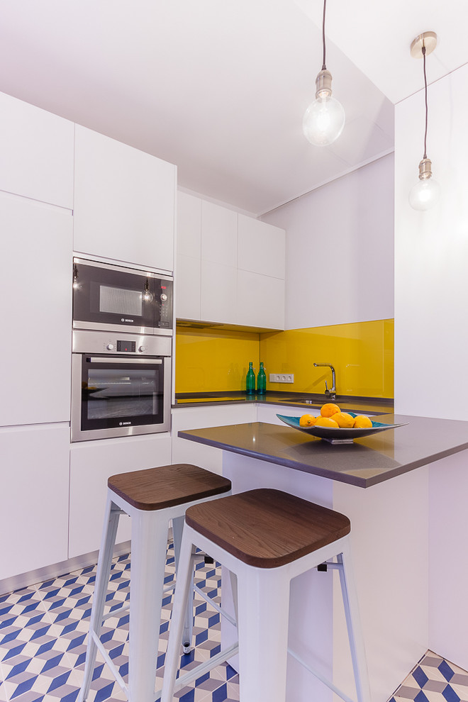 Immagine di una piccola cucina eclettica con ante lisce, ante bianche, paraspruzzi giallo, elettrodomestici in acciaio inossidabile e penisola