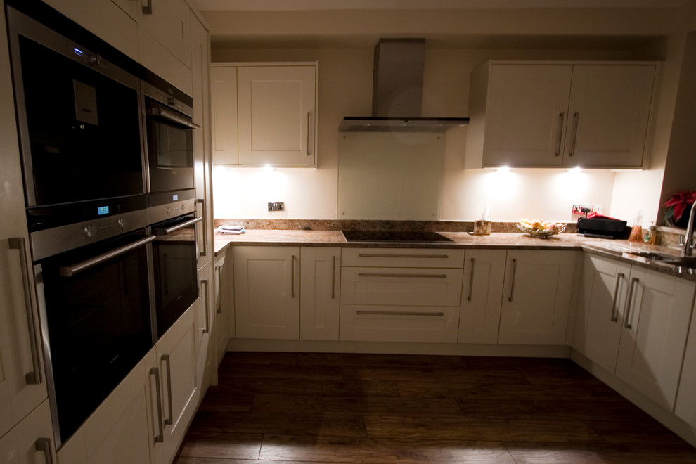 Exempel på ett mellanstort modernt kök, med en integrerad diskho, luckor med infälld panel, vita skåp, granitbänkskiva, vitt stänkskydd, glaspanel som stänkskydd och rostfria vitvaror