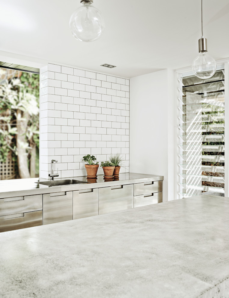 Foto på ett industriellt kök, med släta luckor, skåp i rostfritt stål, bänkskiva i betong, vitt stänkskydd, stänkskydd i tunnelbanekakel, rostfria vitvaror, mellanmörkt trägolv och brunt golv