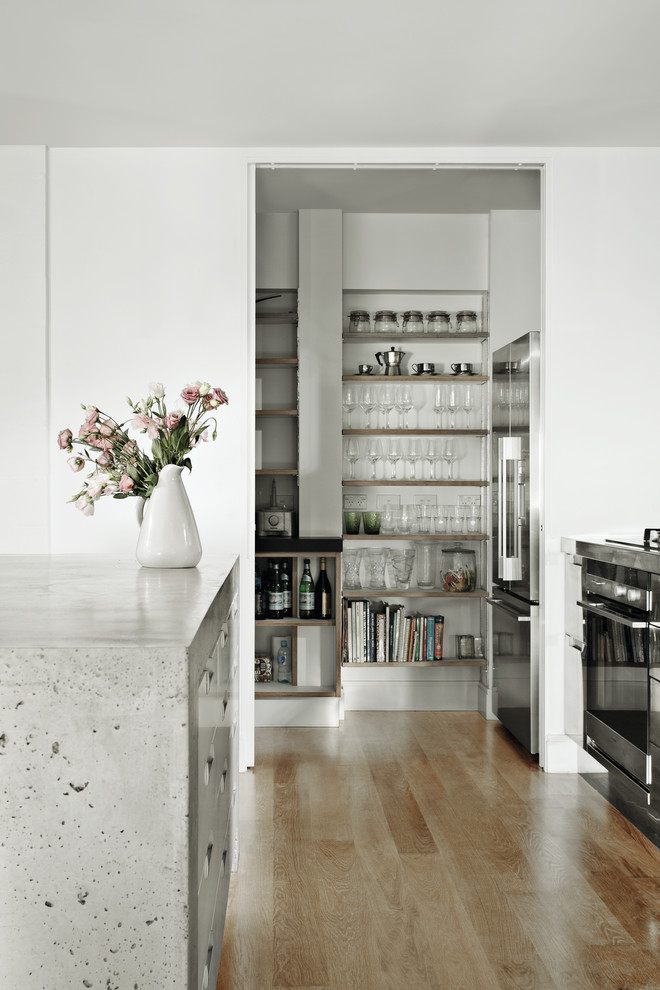 Inspiration for an industrial kitchen pantry with flat-panel cabinets, stainless steel cabinets, concrete worktops, white splashback, metro tiled splashback, stainless steel appliances, medium hardwood flooring and brown floors.