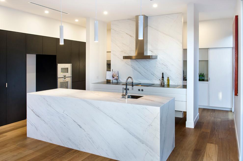 Moderne Küche mit Unterbauwaschbecken, flächenbündigen Schrankfronten, Küchenrückwand in Weiß, weißen Elektrogeräten, braunem Holzboden und Kücheninsel in Melbourne