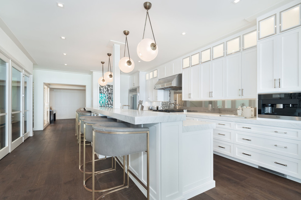 Example of a large beach style u-shaped dark wood floor and brown floor open concept kitchen design in Los Angeles with an undermount sink, recessed-panel cabinets, white cabinets, marble countertops, multicolored backsplash, glass sheet backsplash, stainless steel appliances, an island and white countertops