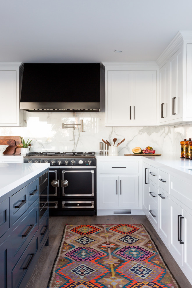 Moderne Küche in L-Form mit Schrankfronten im Shaker-Stil, weißen Schränken, Küchenrückwand in Weiß, schwarzen Elektrogeräten, dunklem Holzboden, Kücheninsel, braunem Boden und weißer Arbeitsplatte in Los Angeles