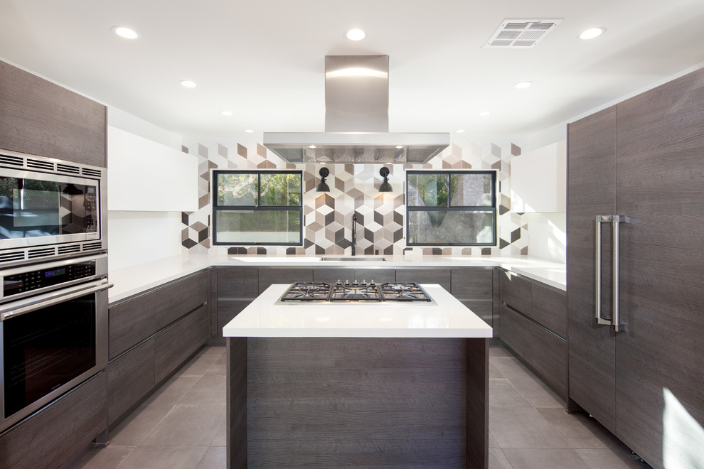 Photo of a medium sized farmhouse u-shaped open plan kitchen in Los Angeles with a single-bowl sink, flat-panel cabinets, dark wood cabinets, composite countertops, grey splashback, ceramic splashback, stainless steel appliances, ceramic flooring, an island, grey floors and white worktops.
