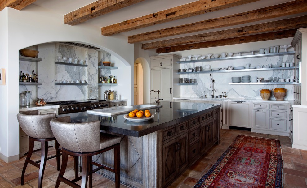 Photo of a mediterranean u-shaped enclosed kitchen in Los Angeles with a built-in sink, recessed-panel cabinets, beige cabinets, marble splashback, stainless steel appliances, terracotta flooring, an island and red floors.