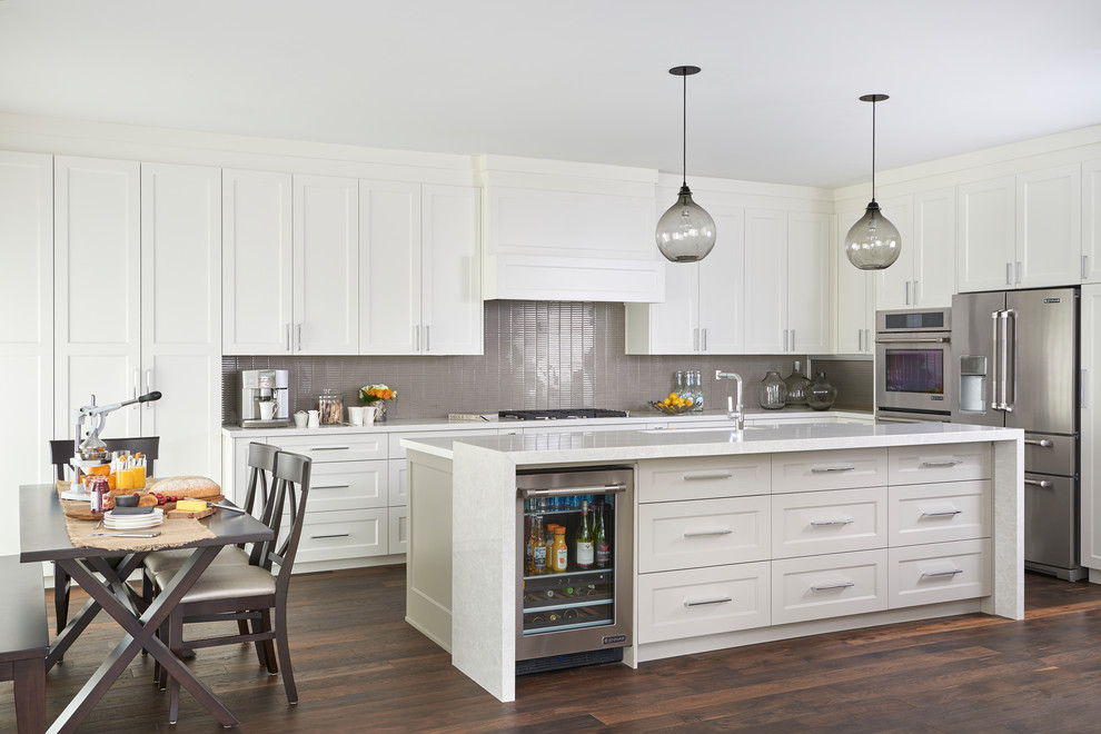 Inspiration for a medium sized traditional grey and cream l-shaped kitchen/diner in Toronto with shaker cabinets, white cabinets, grey splashback, glass tiled splashback, stainless steel appliances, dark hardwood flooring, an island, brown floors, engineered stone countertops and white worktops.