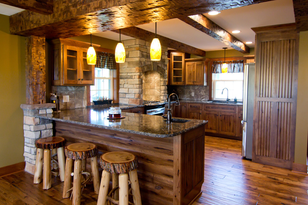 This is an example of a medium sized rustic u-shaped kitchen/diner in Columbus with a submerged sink, shaker cabinets, medium wood cabinets, granite worktops, beige splashback, porcelain splashback, stainless steel appliances, medium hardwood flooring, a breakfast bar, brown floors and multicoloured worktops.