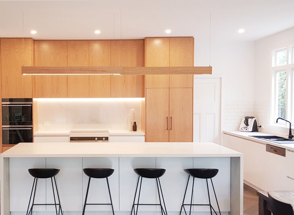 Photo of a medium sized galley kitchen/diner in Melbourne with stone slab splashback, an island, white worktops, a double-bowl sink, flat-panel cabinets, white cabinets, engineered stone countertops, white splashback, stainless steel appliances, dark hardwood flooring and yellow floors.