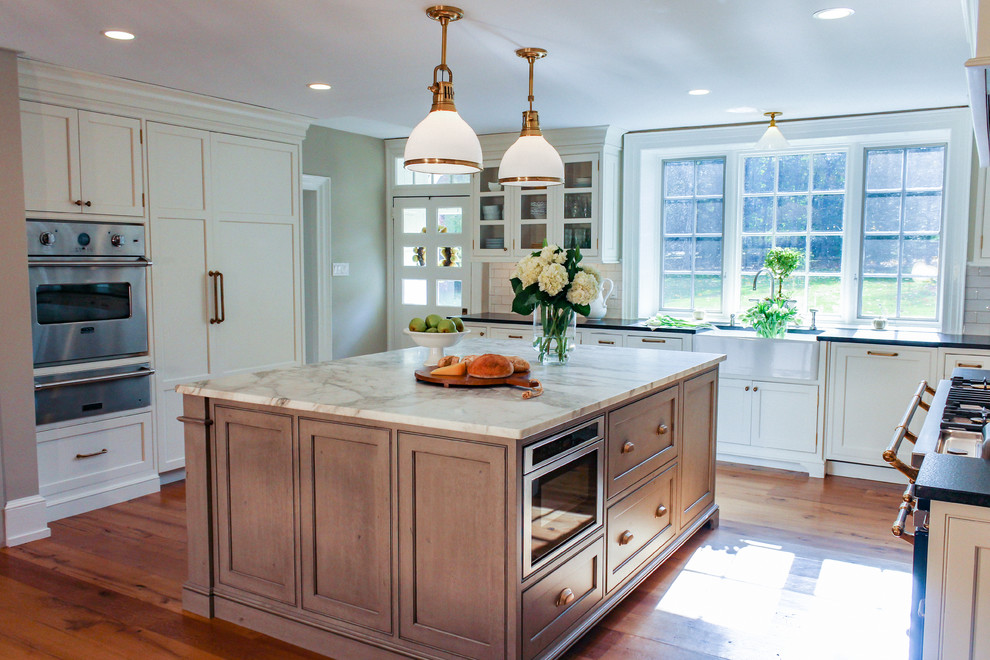 Example of a large cottage l-shaped light wood floor eat-in kitchen design in Philadelphia with a farmhouse sink, beaded inset cabinets, white cabinets, marble countertops, multicolored backsplash, cement tile backsplash, paneled appliances and an island