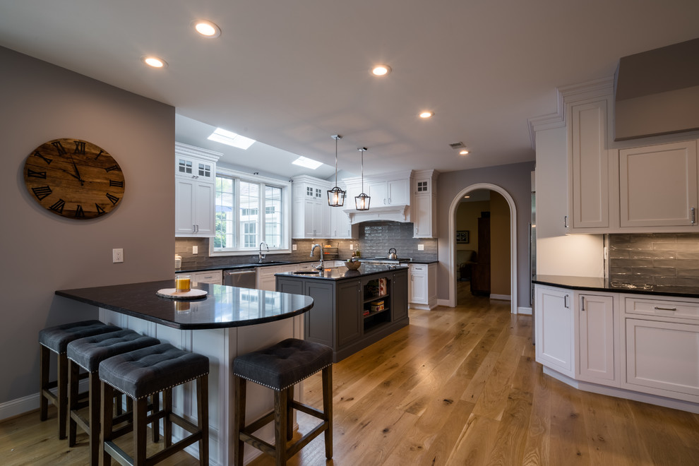 Example of a large transitional l-shaped light wood floor eat-in kitchen design in Philadelphia with an undermount sink, recessed-panel cabinets, white cabinets, gray backsplash, stainless steel appliances and an island