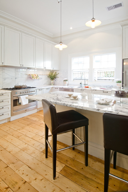 Example of a mid-sized classic l-shaped light wood floor open concept kitchen design in Melbourne with a double-bowl sink, shaker cabinets, white cabinets, marble countertops, white backsplash, stone slab backsplash, stainless steel appliances and an island