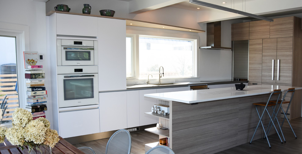 Mid-sized minimalist l-shaped light wood floor eat-in kitchen photo in New York with an undermount sink, flat-panel cabinets, white cabinets, solid surface countertops, white appliances and an island