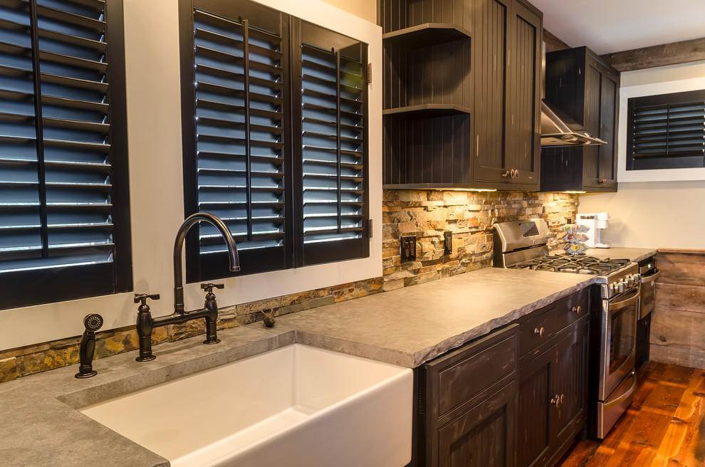 Foto på ett mellanstort lantligt kök, med en rustik diskho, luckor med profilerade fronter, svarta skåp, granitbänkskiva, beige stänkskydd, stänkskydd i stenkakel, rostfria vitvaror, mellanmörkt trägolv och en halv köksö