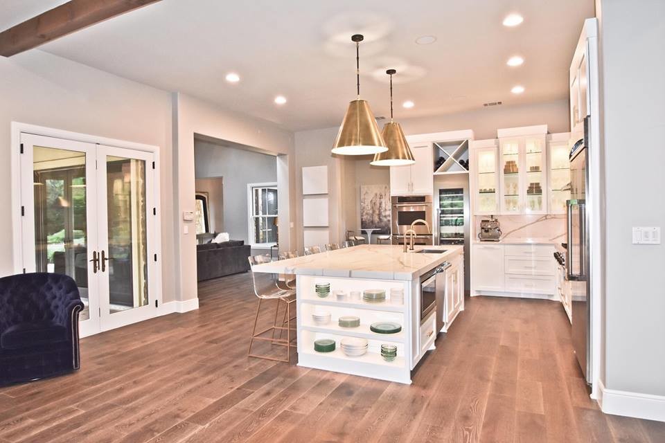 Photo of a medium sized contemporary l-shaped open plan kitchen in Austin with a submerged sink, shaker cabinets, white cabinets, engineered stone countertops, white splashback, stainless steel appliances, medium hardwood flooring, an island, brown floors, white worktops and stone slab splashback.