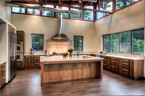 Modern inredning av ett stort kök, med en undermonterad diskho, släta luckor, skåp i mellenmörkt trä, granitbänkskiva, grått stänkskydd, stänkskydd i stenkakel, rostfria vitvaror, klinkergolv i porslin och en köksö