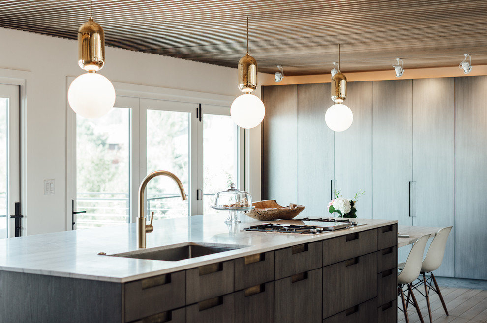 Foto di una cucina minimalista di medie dimensioni con lavello da incasso, ante lisce, ante grigie, top in quarzite, elettrodomestici in acciaio inossidabile, parquet chiaro e penisola