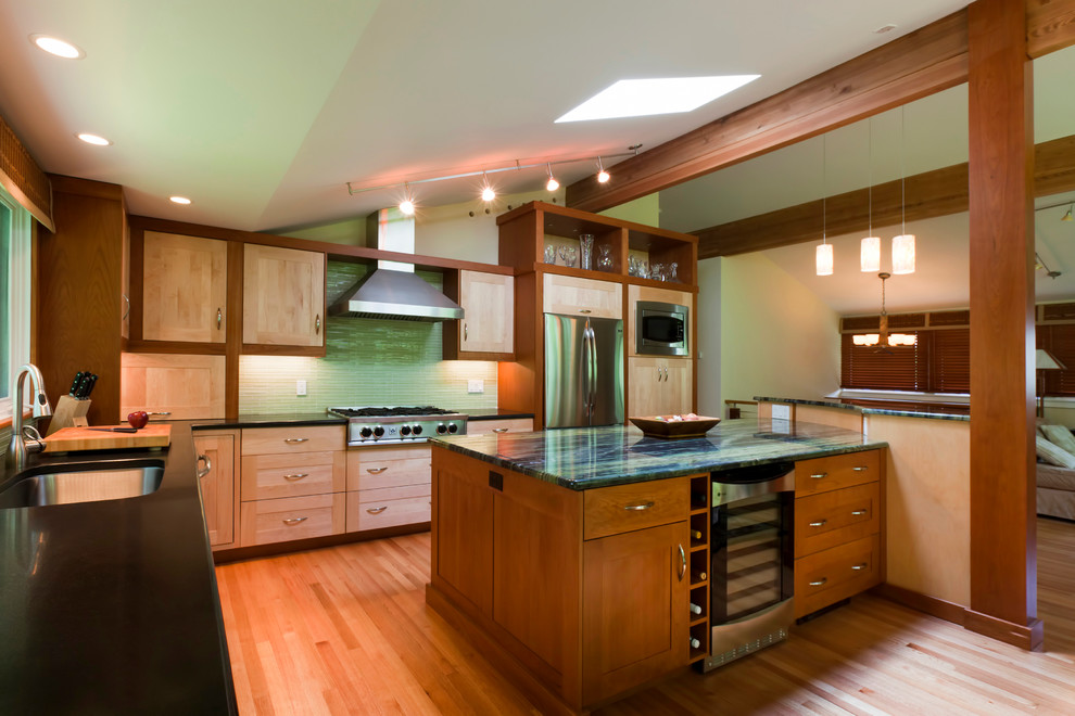 Inredning av ett modernt kök, med en undermonterad diskho, släta luckor, skåp i mellenmörkt trä, granitbänkskiva, grönt stänkskydd och rostfria vitvaror