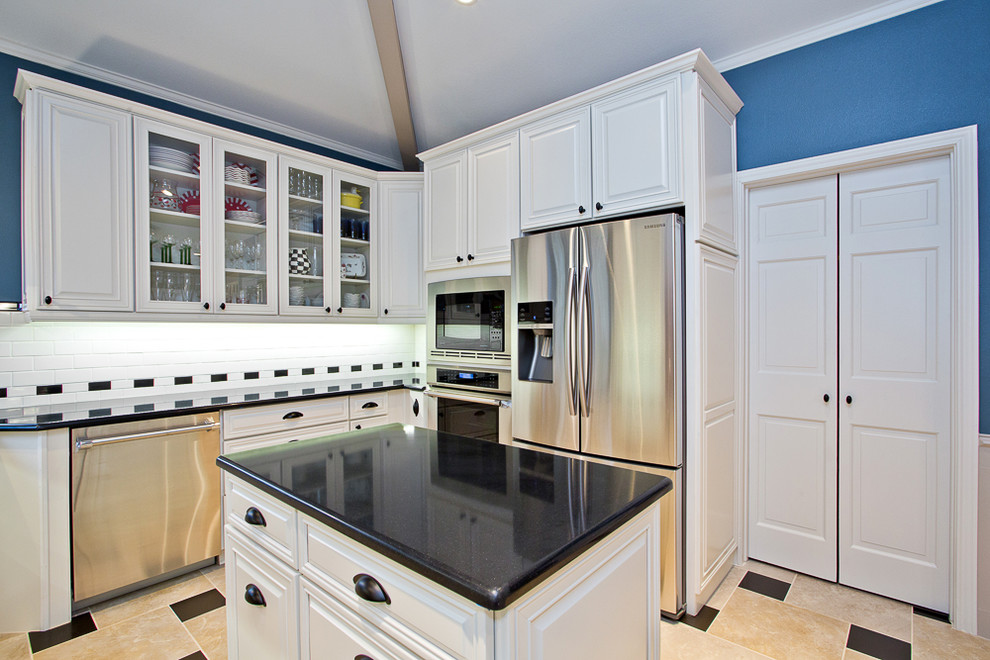 Example of a mid-sized country u-shaped ceramic tile enclosed kitchen design in Dallas with a farmhouse sink, raised-panel cabinets, white cabinets, solid surface countertops, white backsplash, glass tile backsplash, stainless steel appliances and an island